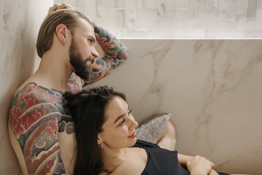 Close-up of a tattooed man and woman relaxing together indoors in a serene setting.